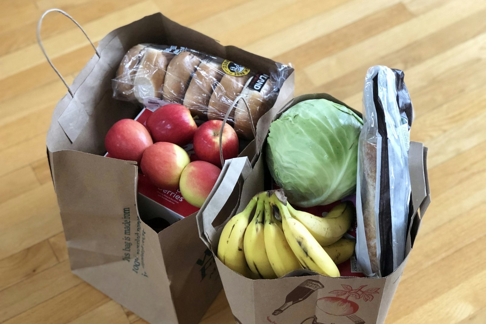 Two paper bags of shopping with apples, bananas, bread and a cabbage