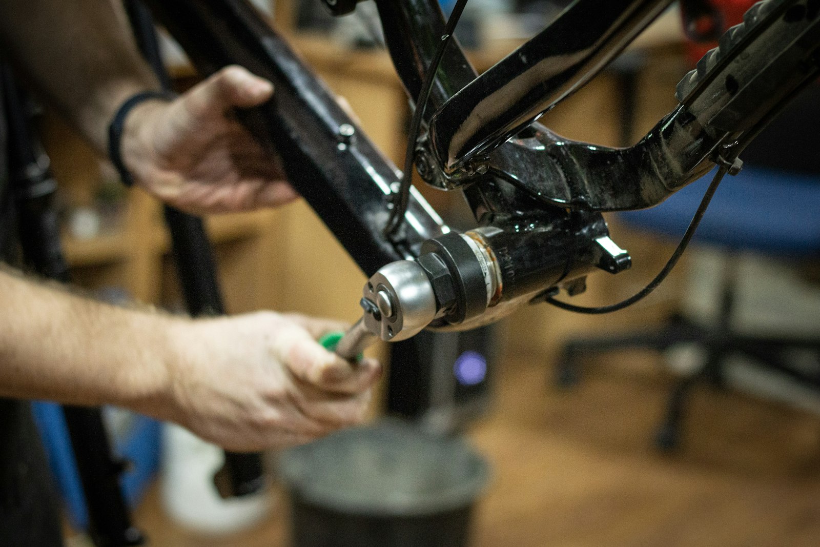 A mechanic's hands working on the bottom bracket of a bike frame in a workshop