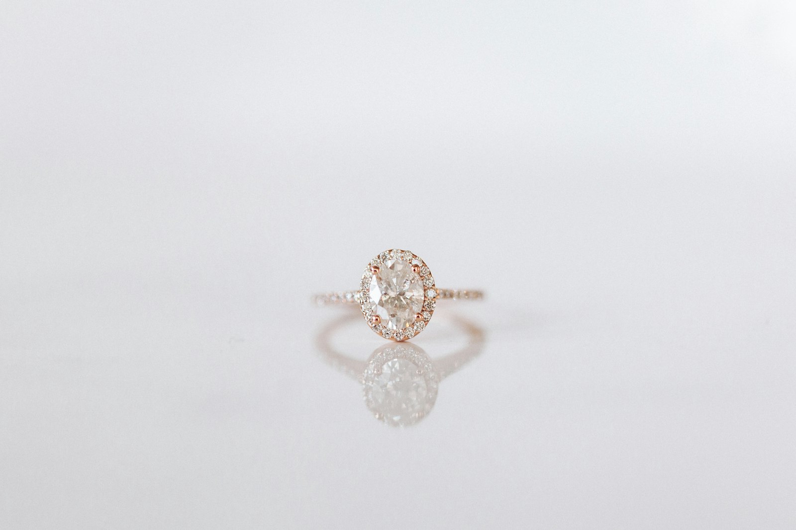 Oval diamond halo engagement ring in rose gold on a white surface