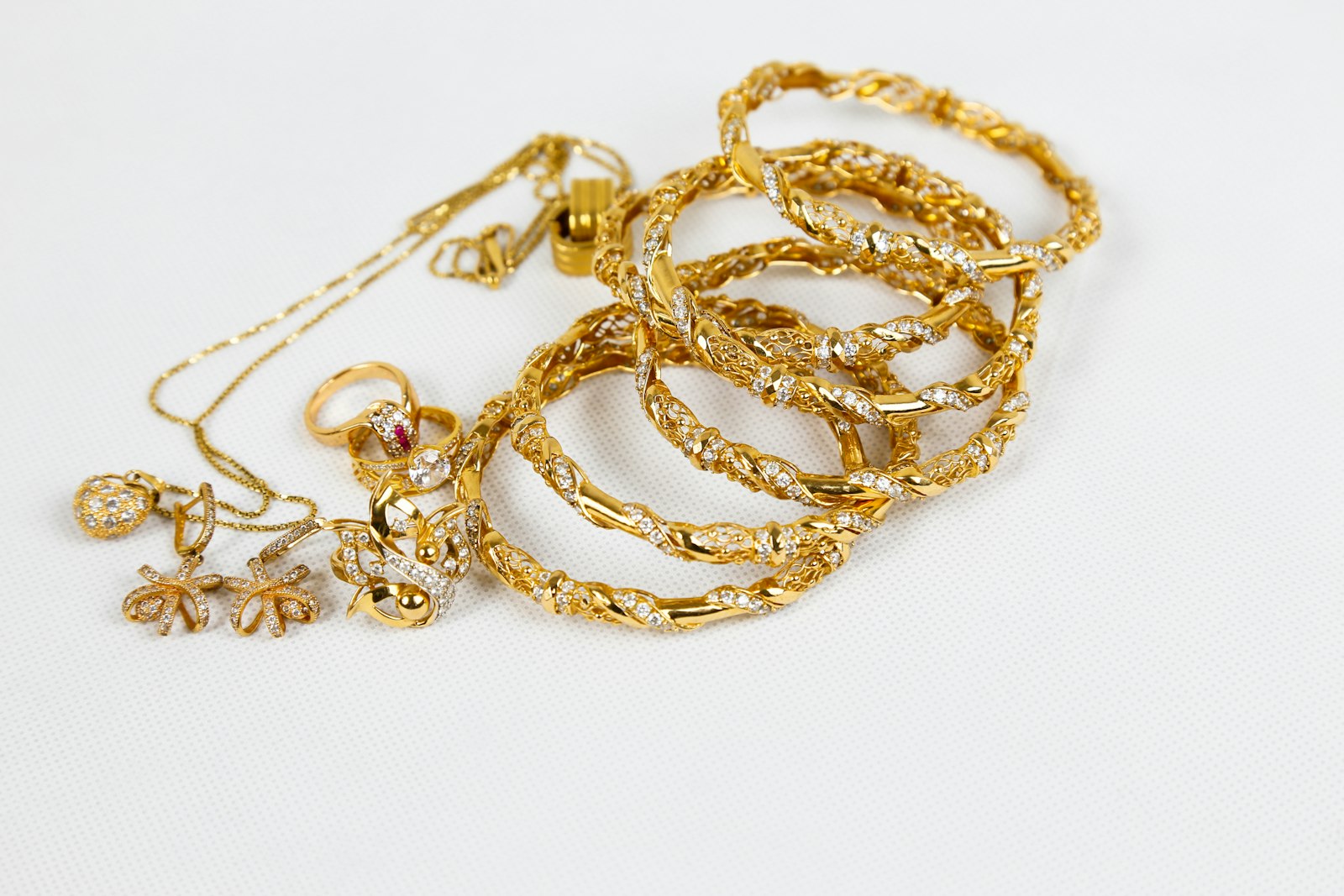 Gold bangles, rings, earrings and a chain necklace on a white surface