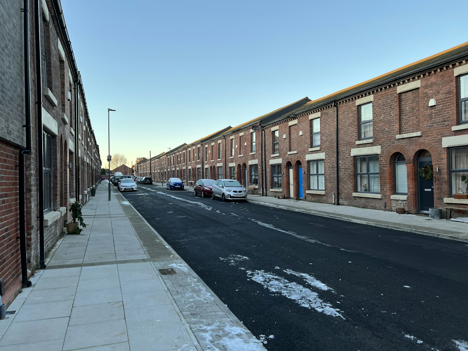 A street of red-brick terraced houses with parked cars under a clear winter sky