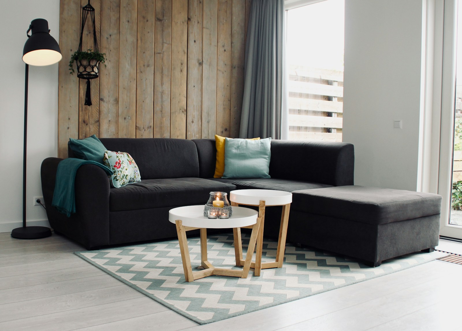 Grey corner sofa with cushions, two round coffee tables and a patterned rug in a bright living room
