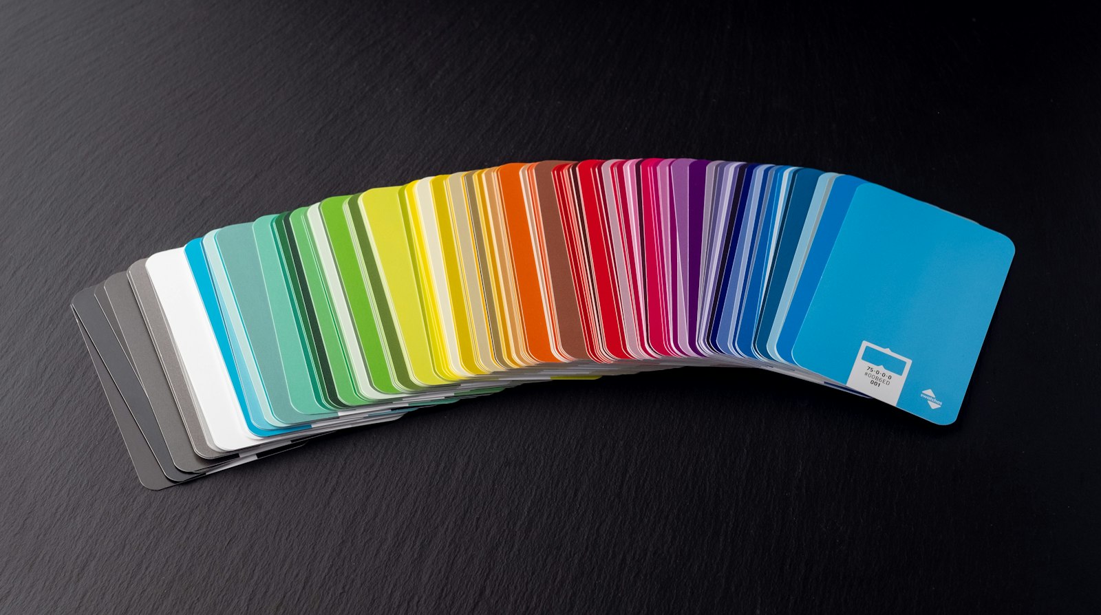 Fan of rainbow-coloured material sample cards on a dark slate surface