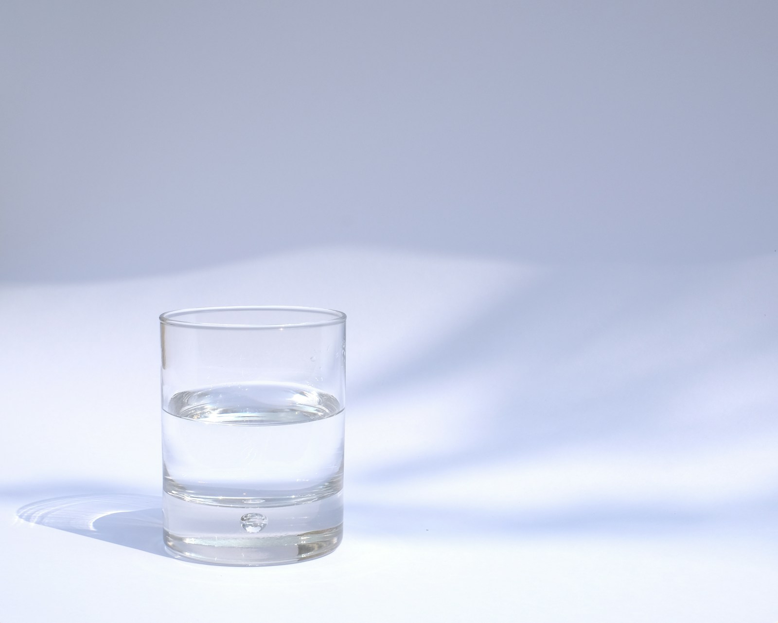 A clear glass half filled with water on a white surface in soft light