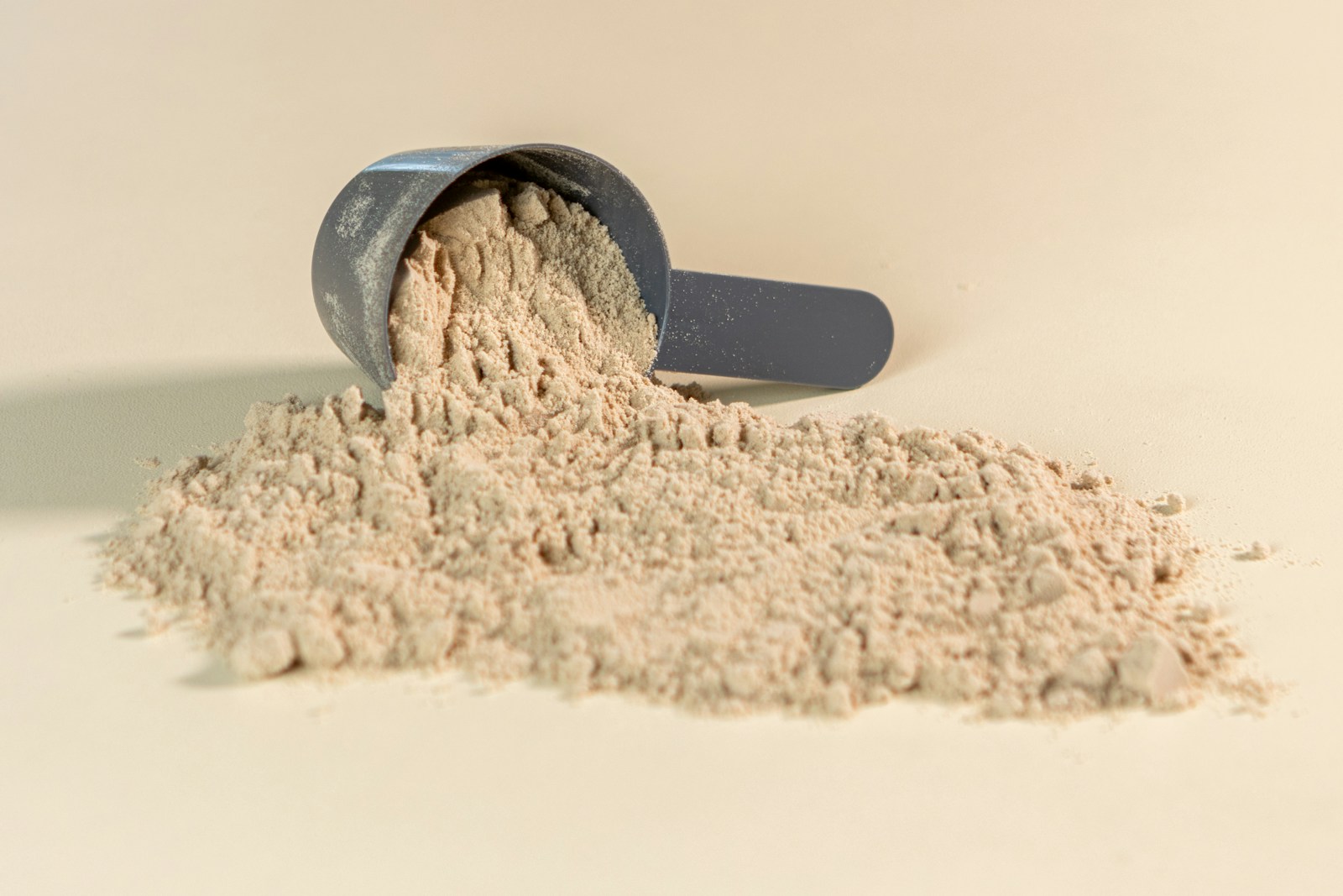 A scoop tipped over with protein powder spilling across a pale table