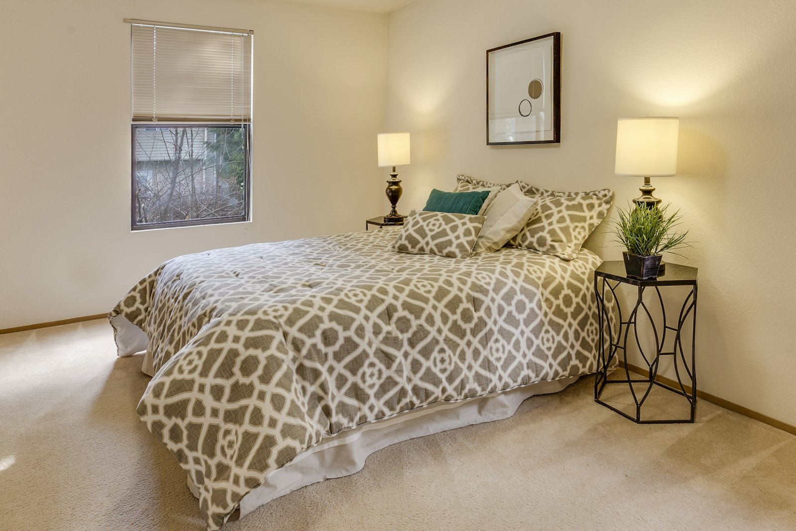 A neatly made bed with a patterned bedspread beside a bright window