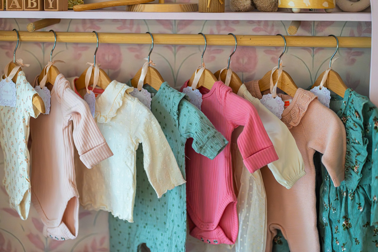 Pastel baby bodysuits and tops hanging on wooden hangers on a nursery rail