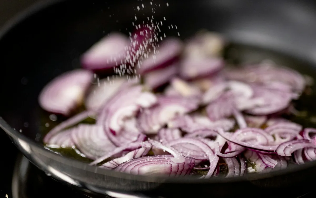 Sliced red onions being salted in a frying pan Sliced red onions being salted in a frying pan