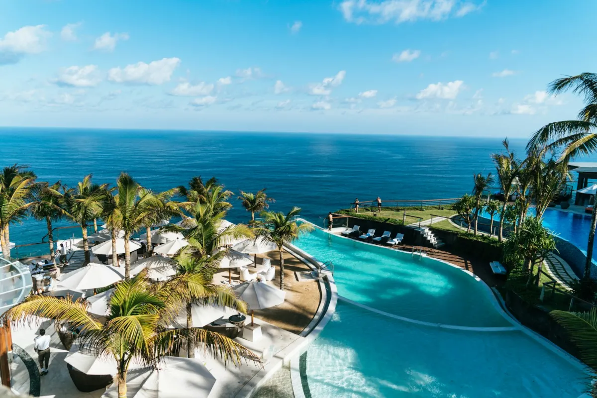 Clifftop resort pool lined with palm trees and parasols overlooking the ocean in Bali Clifftop resort pool lined with palm trees and parasols overlooking the ocean in Bali