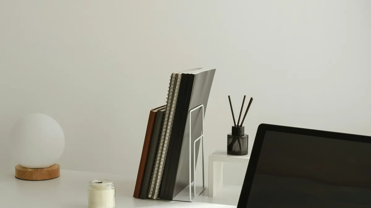 Minimal white desk with a laptop, notebooks in a rack, a globe lamp and a candle