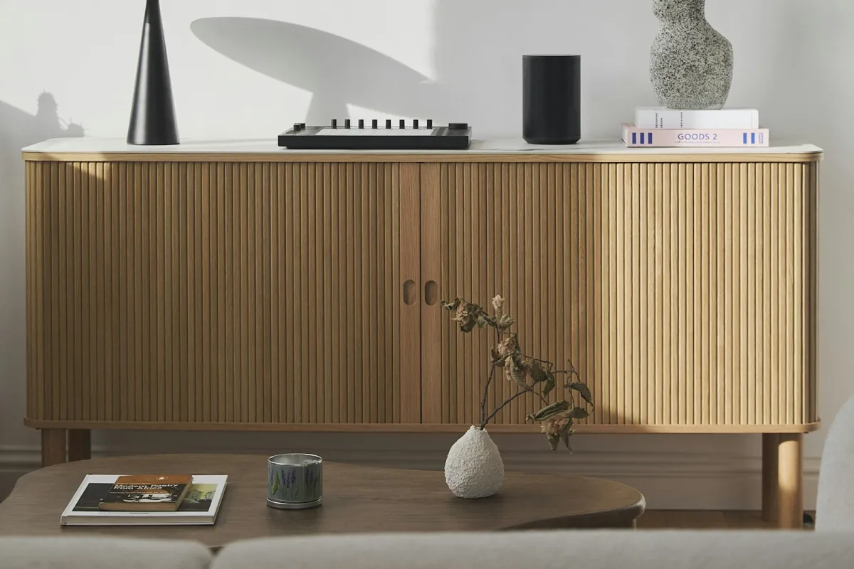 A wooden sideboard styled with a vase, books and ornaments behind a coffee table in a bright living room A wooden sideboard styled with a vase, books and ornaments behind a coffee table in a bright living room