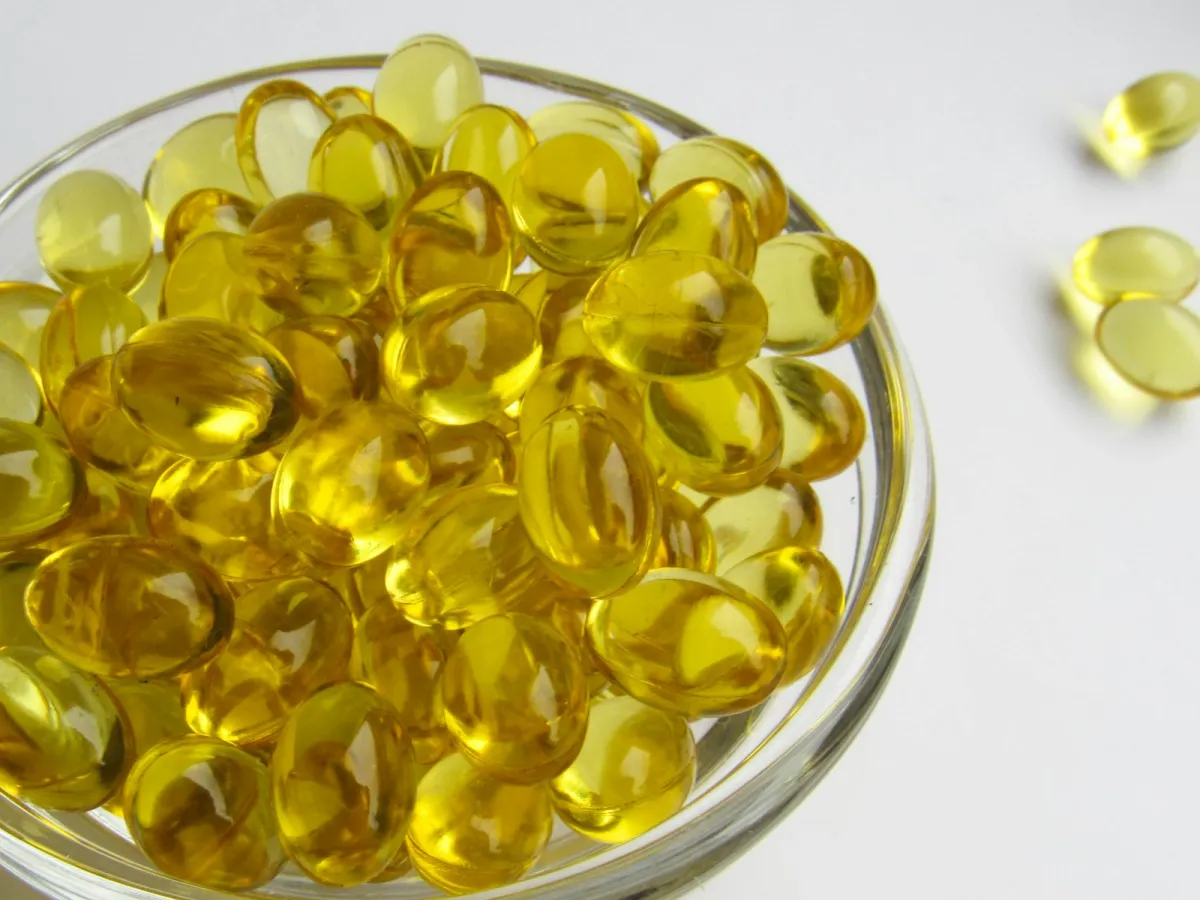 A glass bowl full of golden softgel capsules on a white table A glass bowl full of golden softgel capsules on a white table