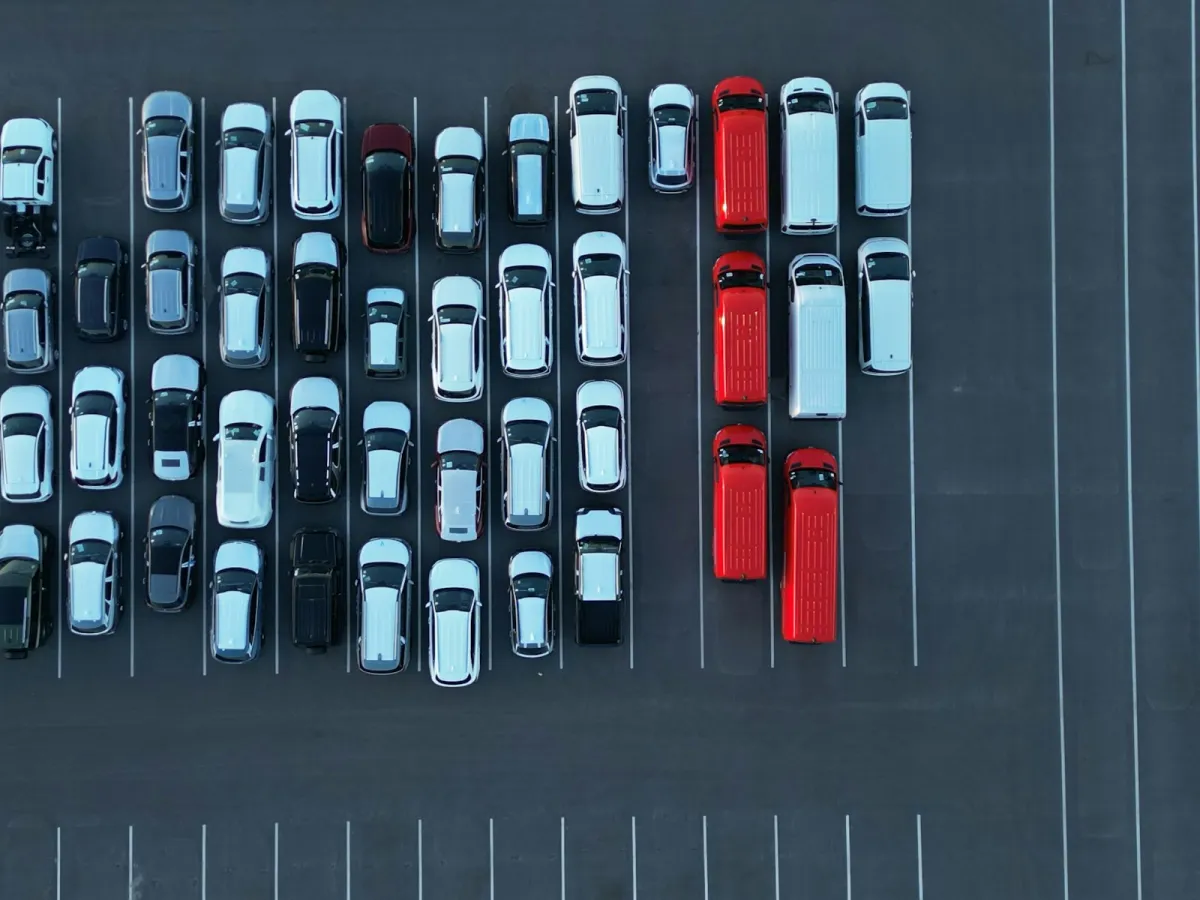 Aerial view of rows of parked cars and red vans in a large car park Aerial view of rows of parked cars and red vans in a large car park