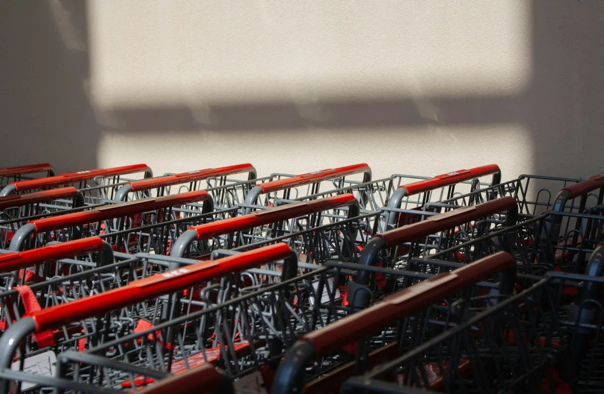 Rows of supermarket trolleys with red handles lined up against a wall