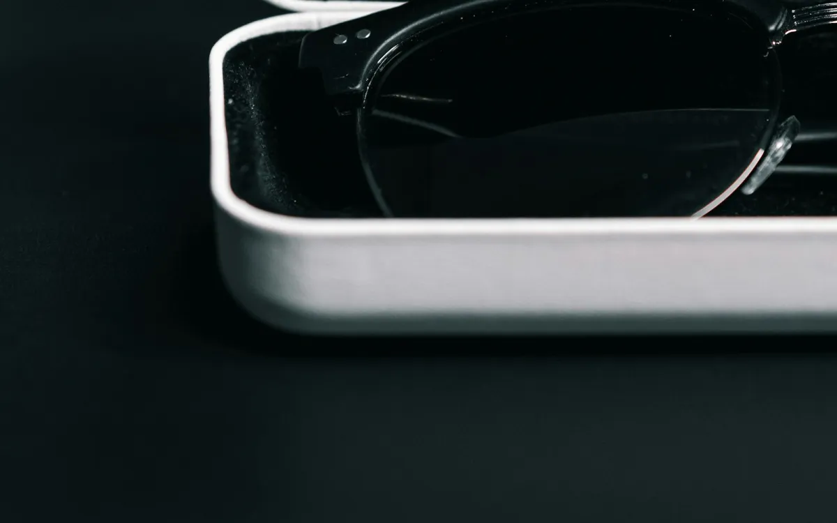 A pair of dark-framed glasses resting in an open white glasses case A pair of dark-framed glasses resting in an open white glasses case