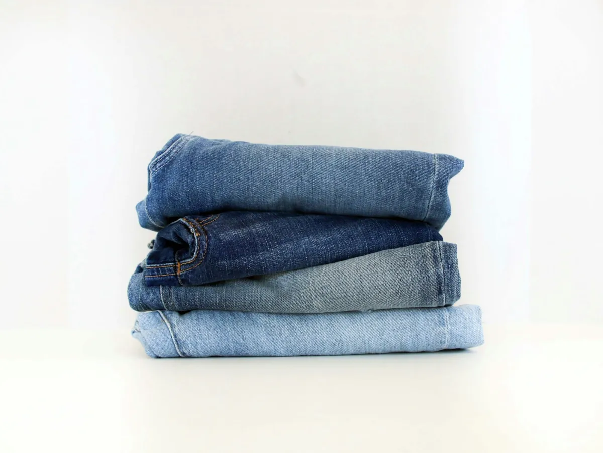 A neat stack of folded blue jeans in different washes on a white background