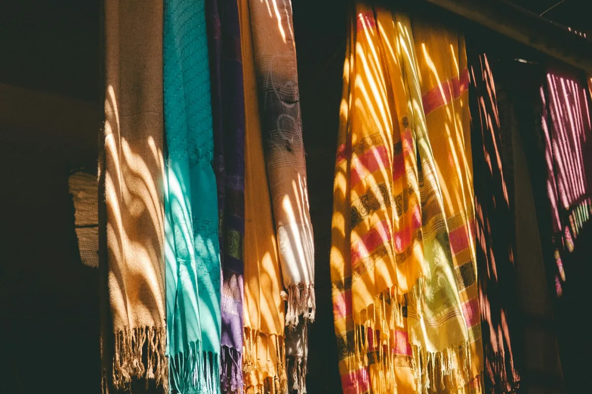 Colourful scarves hanging in a row, lit by strips of sunlight Colourful scarves hanging in a row, lit by strips of sunlight