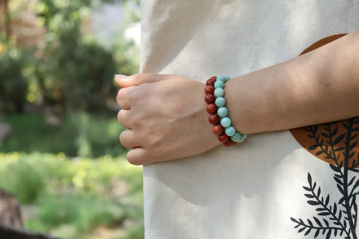 Two beaded bracelets on a wrist against a linen bag