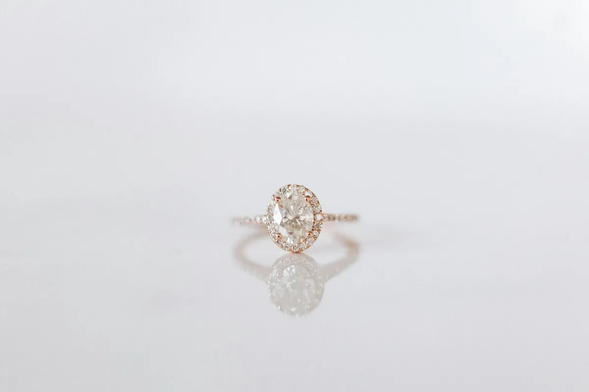 Oval diamond halo engagement ring in rose gold on a white surface