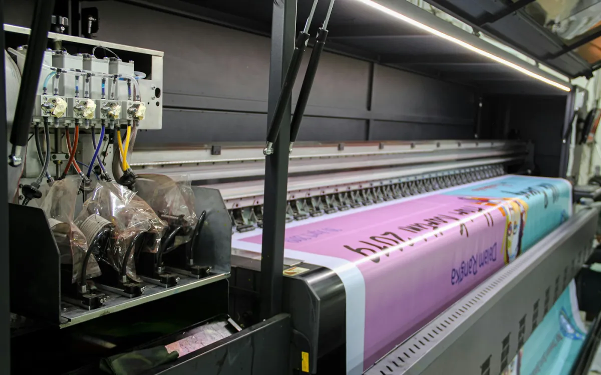 A large-format industrial printer printing a long pink and blue banner