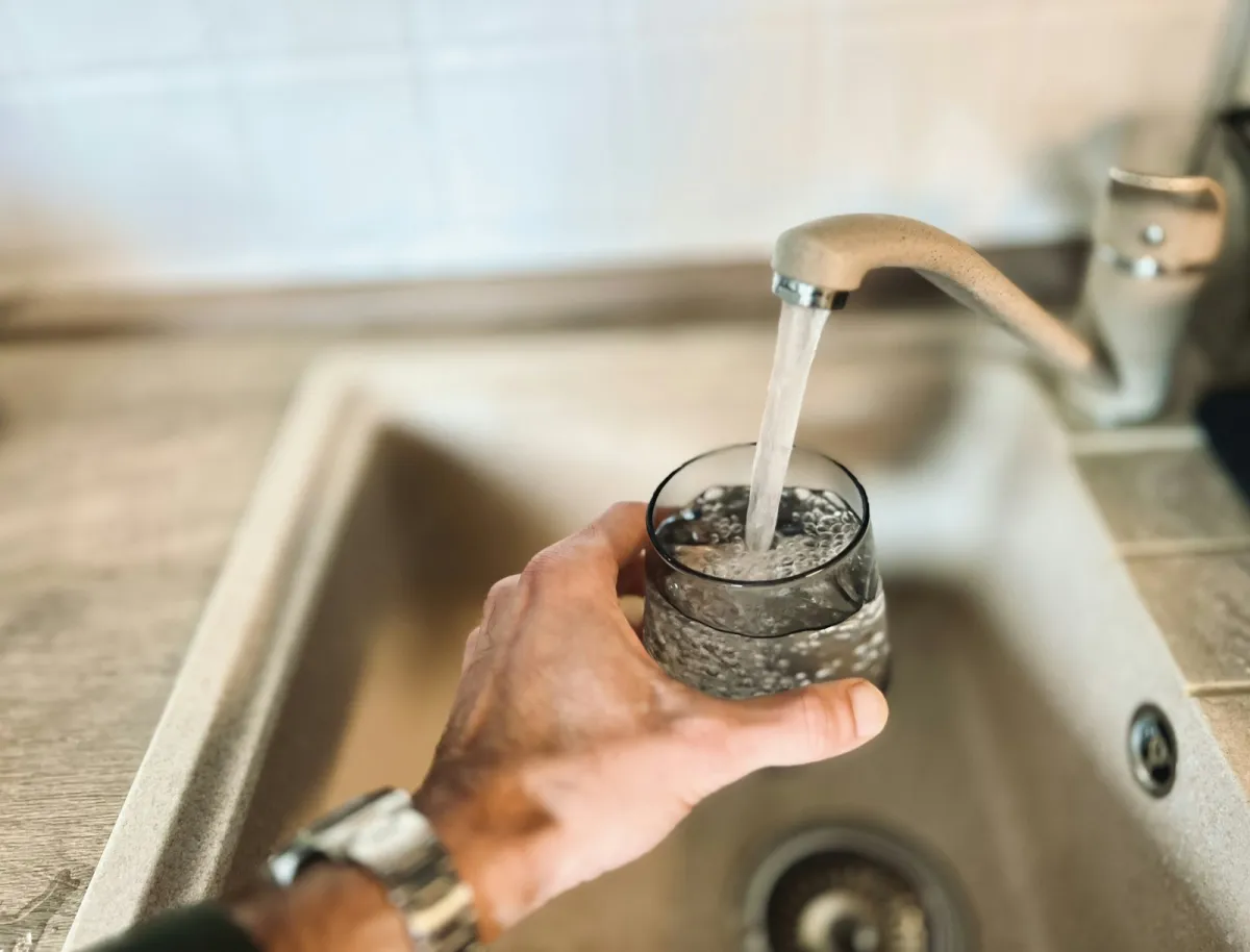 A hand filling a glass with water from a kitchen tap A hand filling a glass with water from a kitchen tap