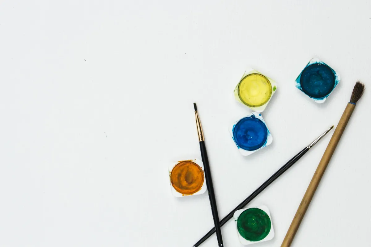 Watercolour paint pots and paintbrushes on a white surface