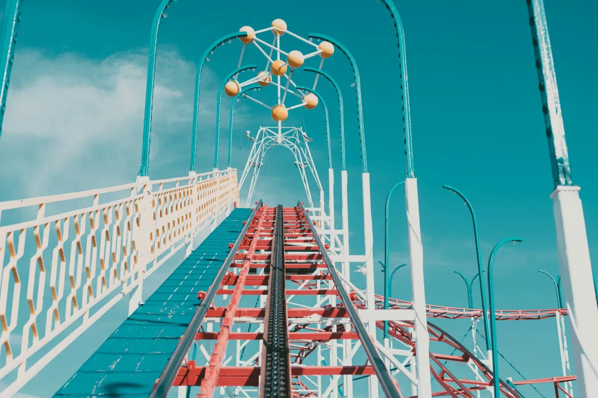 Looking up a red and white roller coaster track against a blue sky