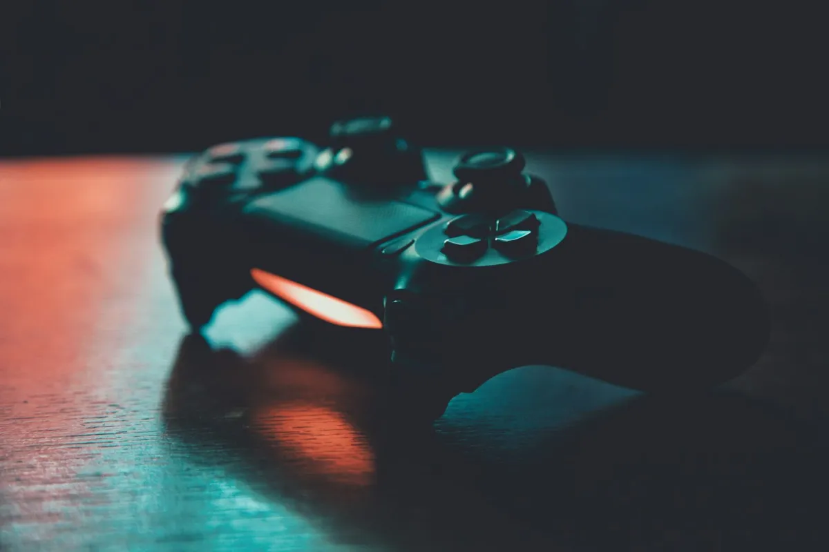 Black game controller on a wooden table lit in blue and orange