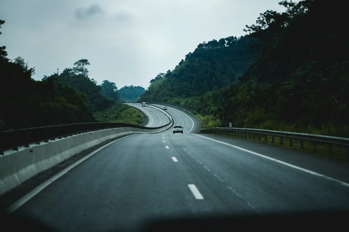 Cars on a quiet winding highway through green wooded hills