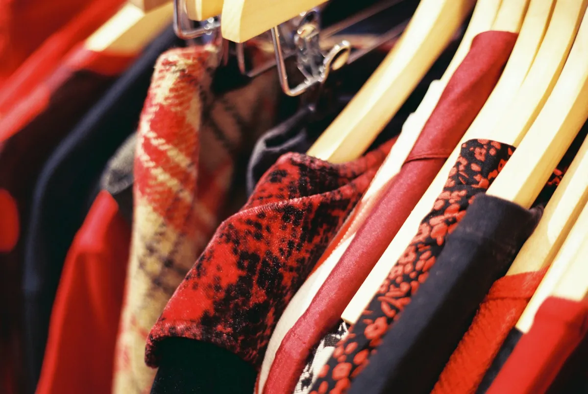 Red and black patterned dresses on wooden hangers along a clothing rail Red and black patterned dresses on wooden hangers along a clothing rail