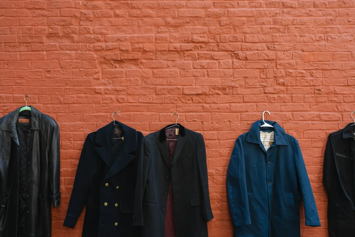 A row of men's coats on hangers against a red brick wall A row of men's coats on hangers against a red brick wall