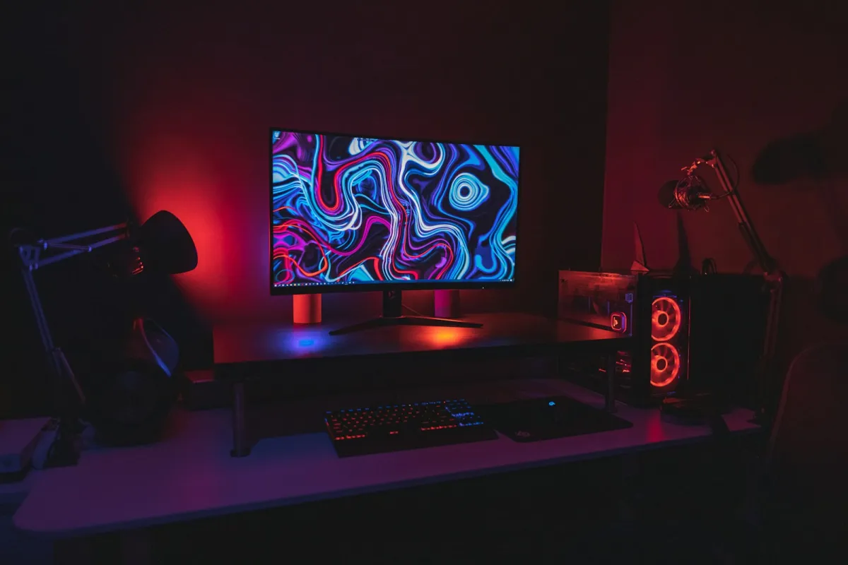 A gaming desk with a curved monitor, keyboard and PC tower lit in red and blue