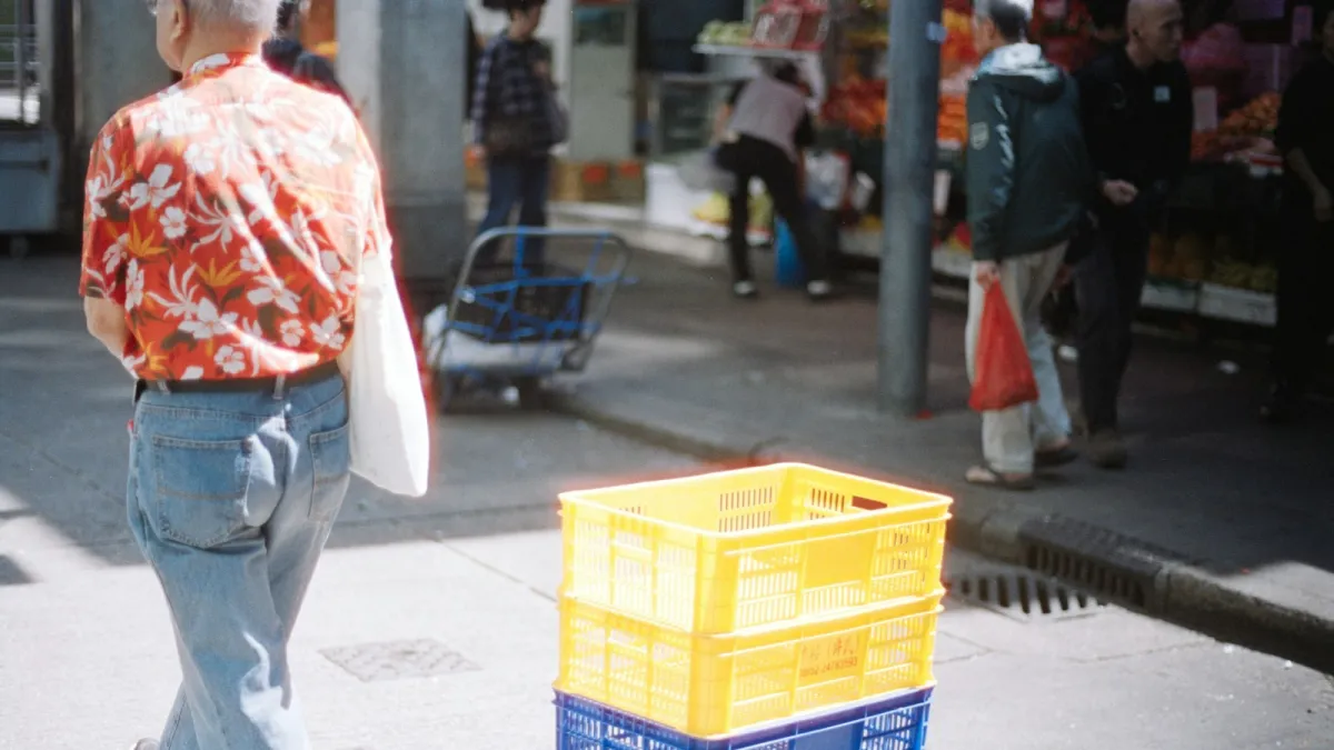 Man in a red floral shirt walking past stacked yellow crates at a street market Man in a red floral shirt walking past stacked yellow crates at a street market