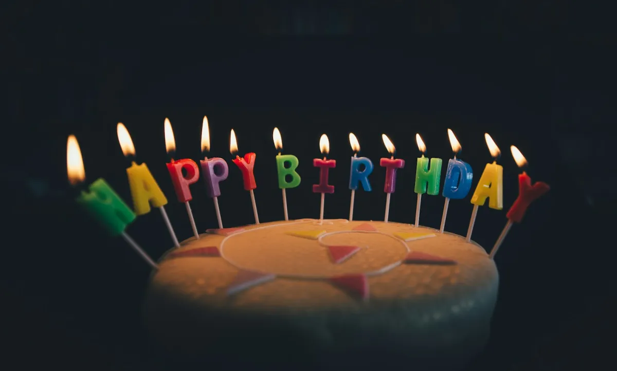 A round iced cake with lit Happy Birthday letter candles against a dark background A round iced cake with lit Happy Birthday letter candles against a dark background