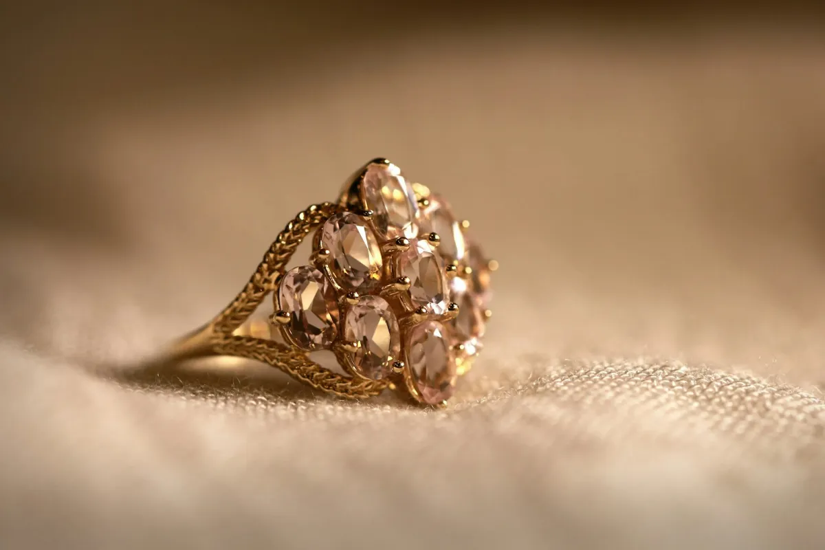 Gold cluster ring set with pale pink stones resting on soft cream fabric Gold cluster ring set with pale pink stones resting on soft cream fabric