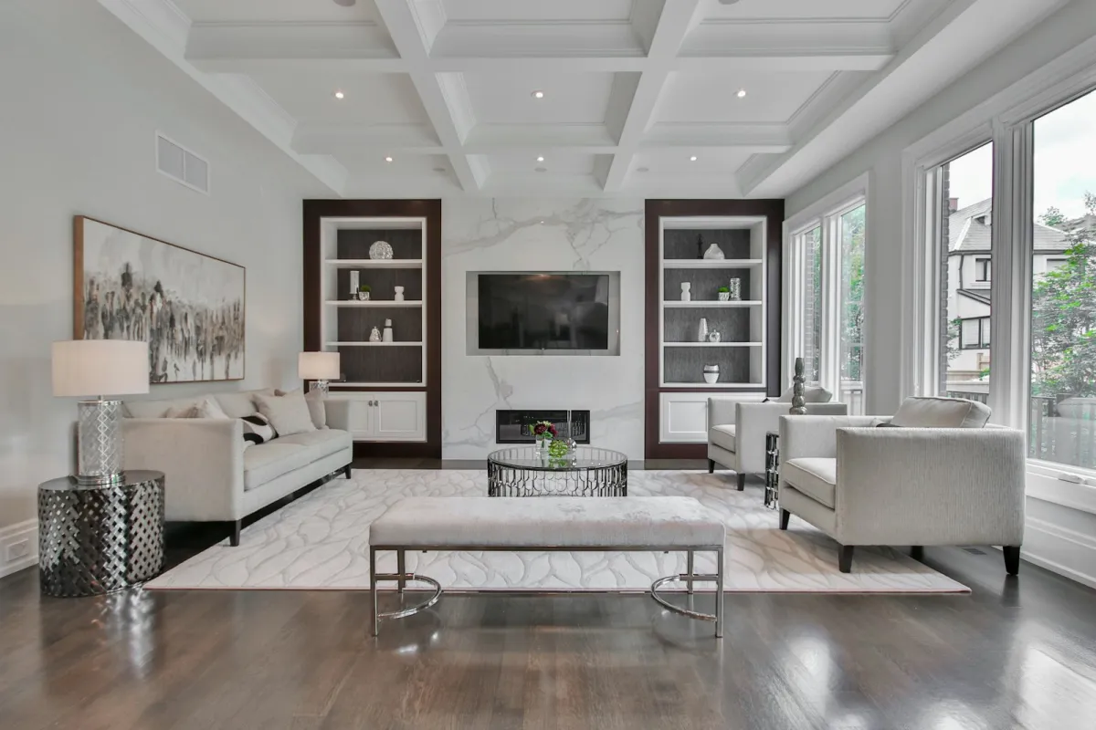 An elegant living room with pale sofas, armchairs, a marble fireplace wall and a coffered ceiling