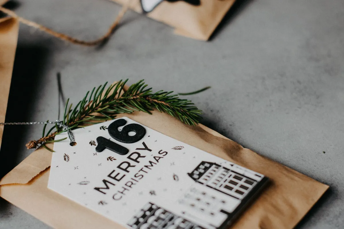 A brown paper advent calendar bag with a number 16 Merry Christmas tag and a sprig of fir on a grey surface A brown paper advent calendar bag with a number 16 Merry Christmas tag and a sprig of fir on a grey surface