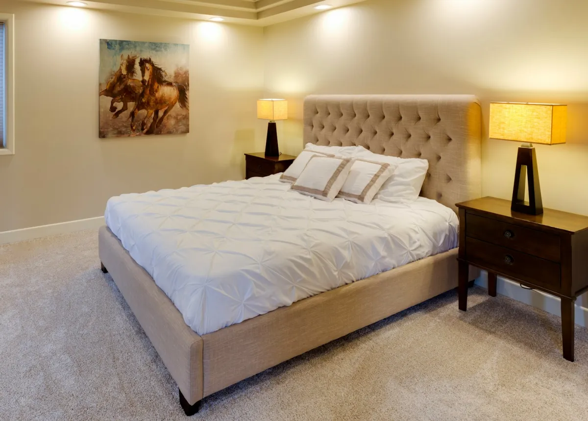 Upholstered bed with a tufted headboard and white bedding between two bedside lamps