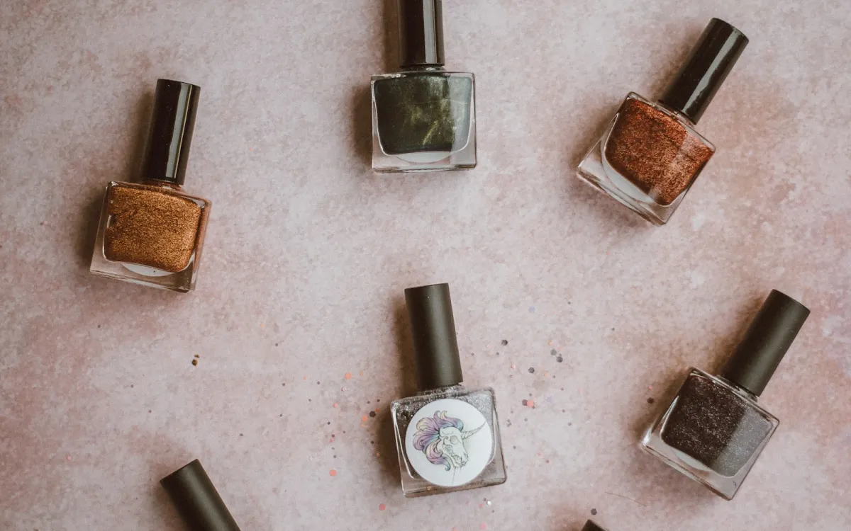 Bottles of glittery brown, green and grey nail polish on a pink surface