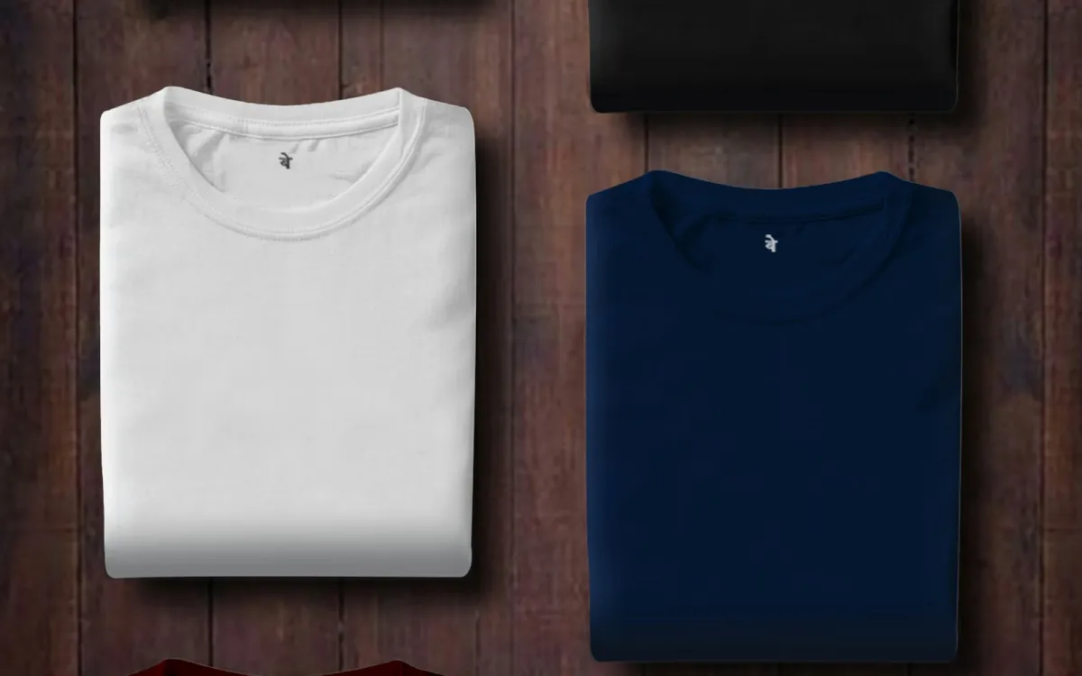 Neatly folded plain T-shirts in white, navy and black on a wooden surface Neatly folded plain T-shirts in white, navy and black on a wooden surface