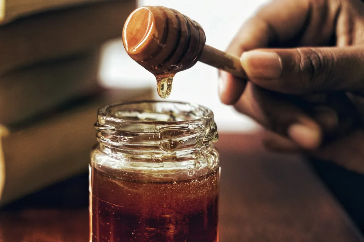 Honey dripping from a wooden dipper into a glass jar Honey dripping from a wooden dipper into a glass jar