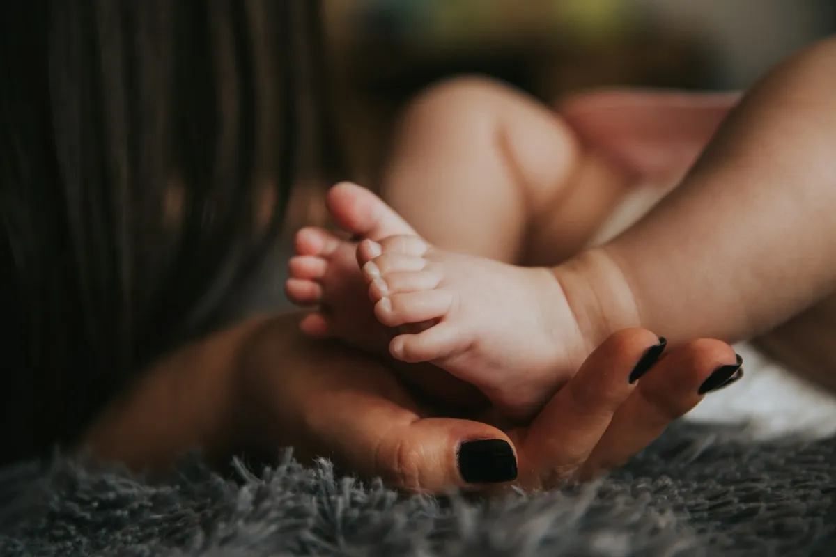 A parent's hand gently holding a baby's feet on a soft grey blanket
