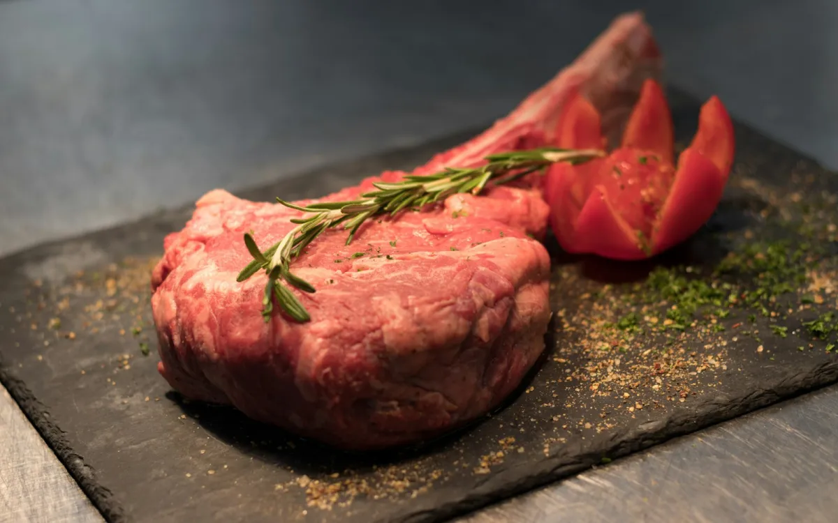 A thick raw steak with rosemary and tomato on a black slate board A thick raw steak with rosemary and tomato on a black slate board