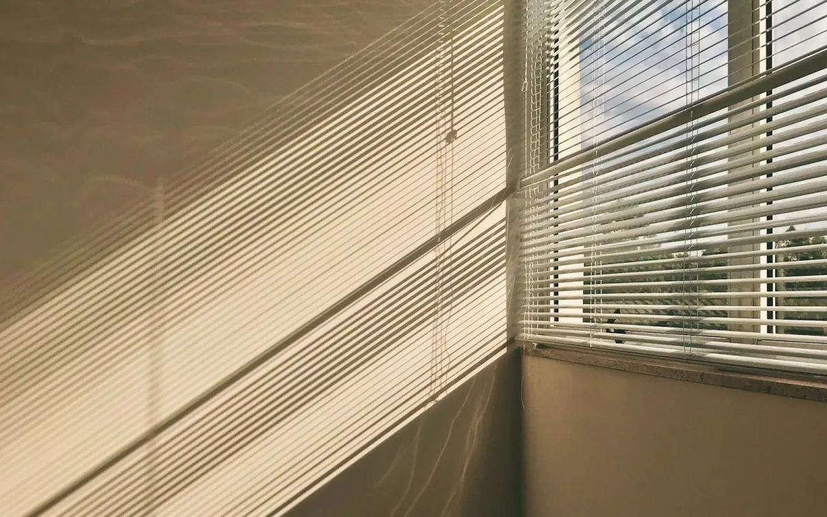 Sunlight falling on a wall through white Venetian blinds at a corner window Sunlight falling on a wall through white Venetian blinds at a corner window