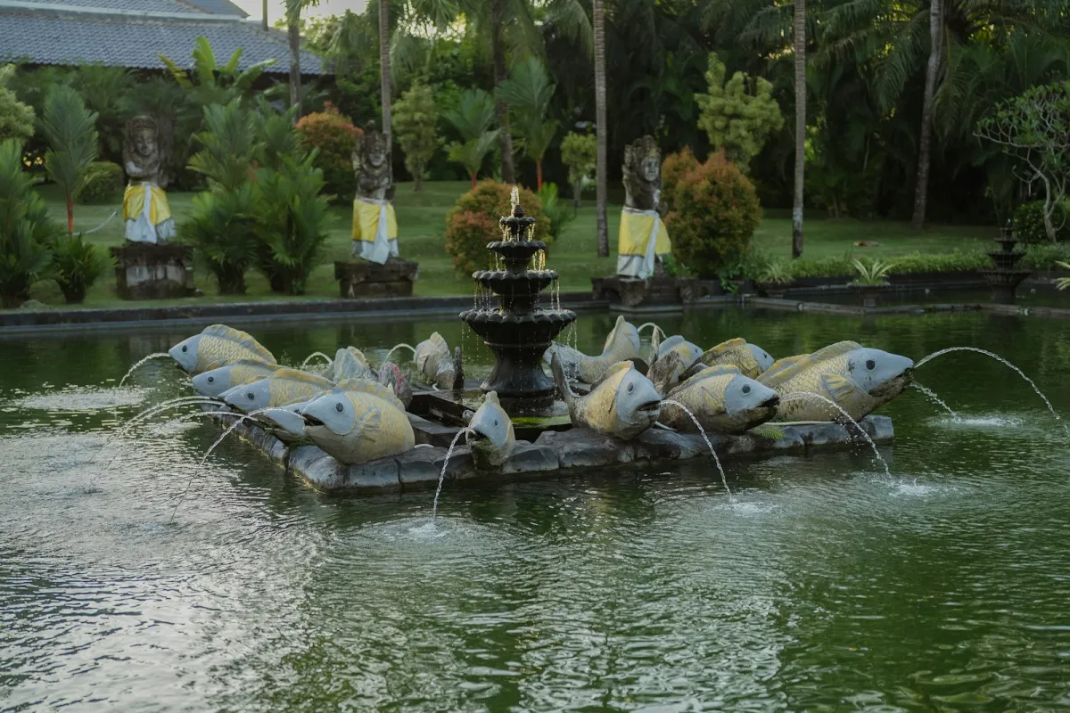 A garden pond with a tiered fountain and fish sculptures spouting water A garden pond with a tiered fountain and fish sculptures spouting water