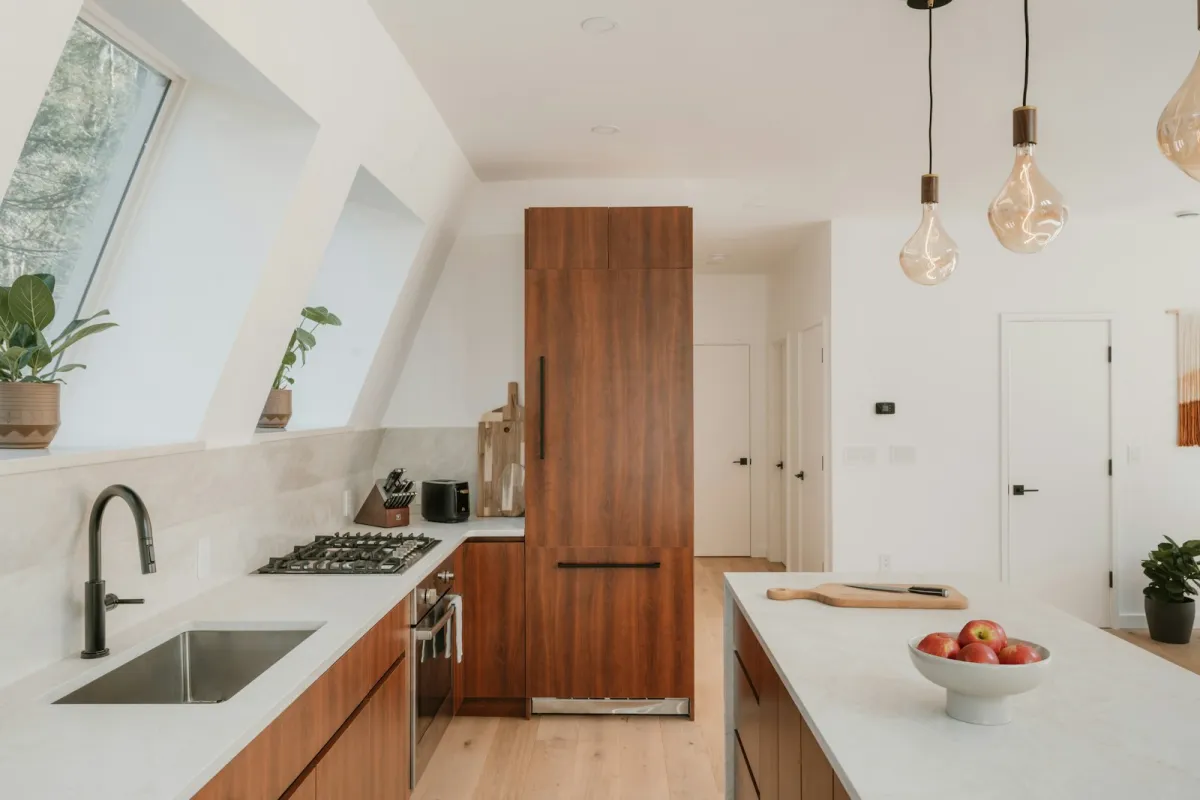 A modern kitchen with wood-effect cabinets, a pale stone worktop and an island under pendant lights A modern kitchen with wood-effect cabinets, a pale stone worktop and an island under pendant lights