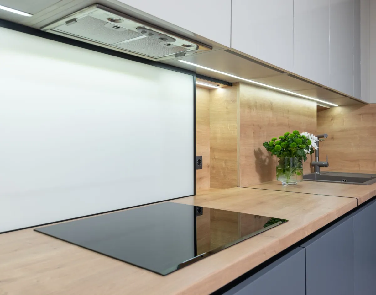 A black glass hob set into a wooden worktop beneath a cooker hood in a modern kitchen A black glass hob set into a wooden worktop beneath a cooker hood in a modern kitchen
