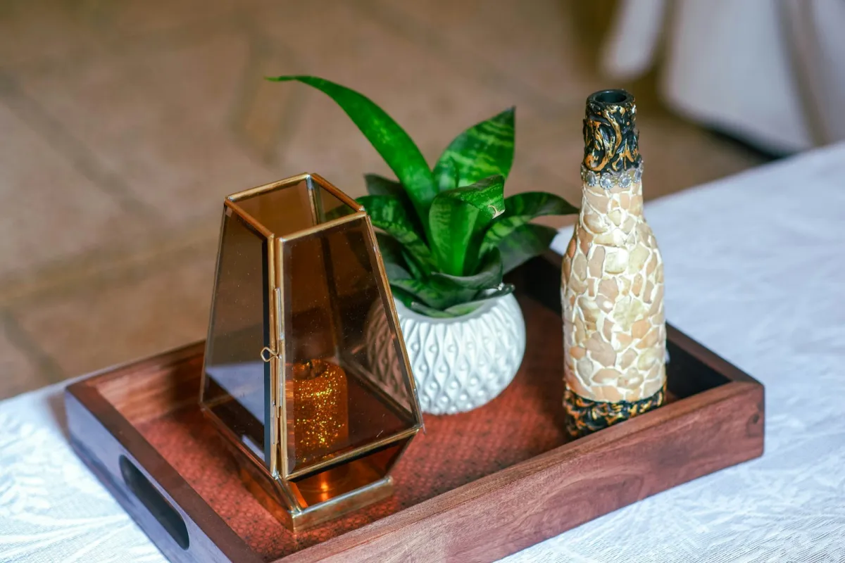 Candle lantern, potted plant and decorative bottle arranged on a wooden tray