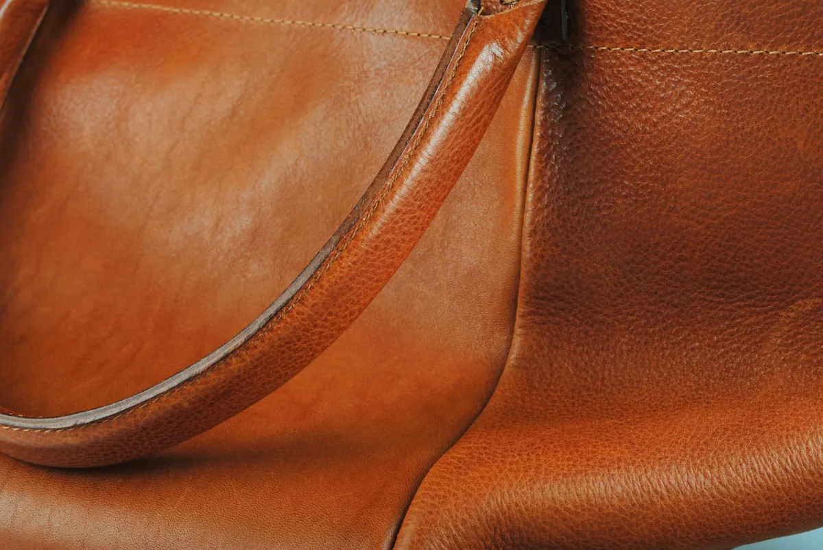 Close-up of a tan leather handbag showing its stitched handle and grained leather Close-up of a tan leather handbag showing its stitched handle and grained leather