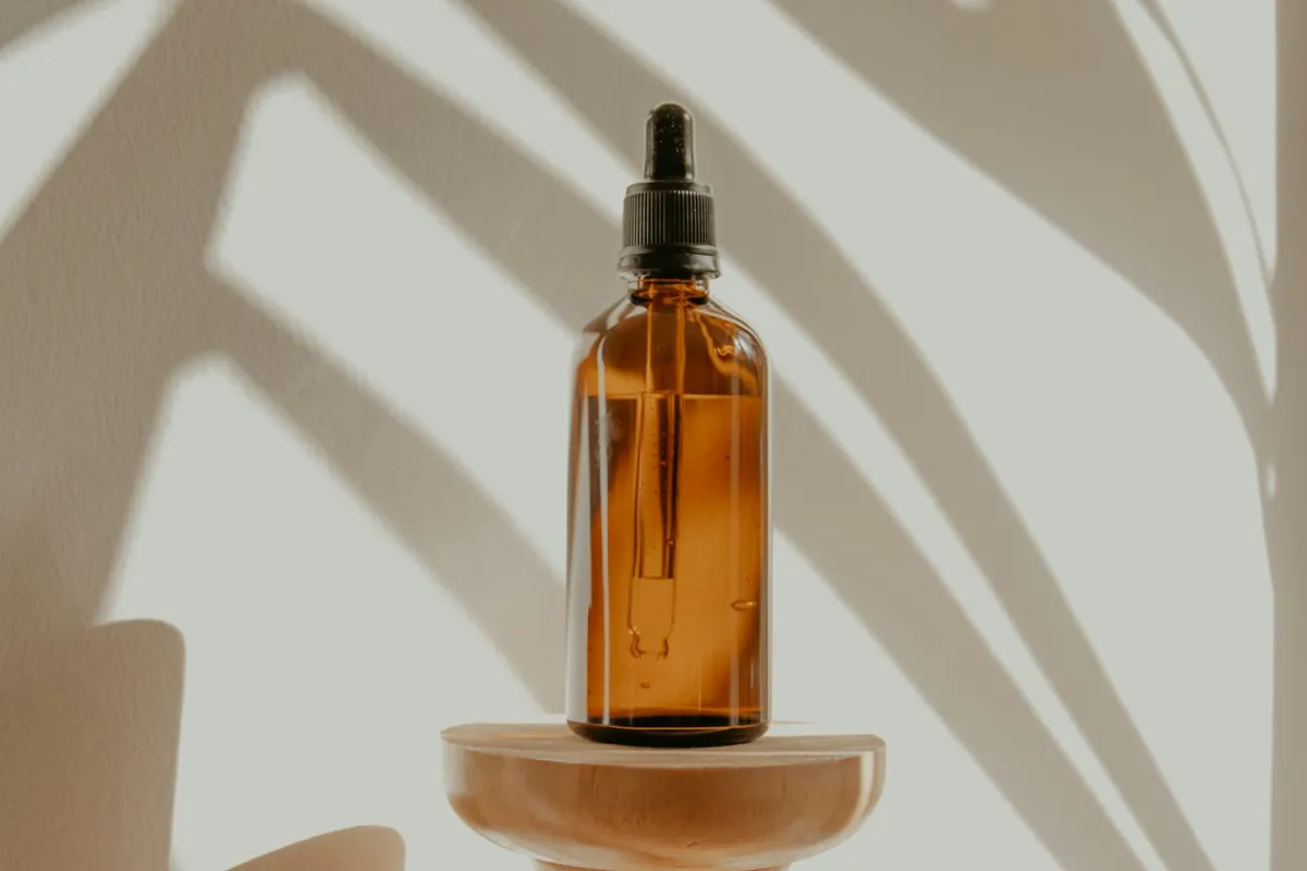 Amber glass dropper bottle on a wooden stand with palm leaf shadows Amber glass dropper bottle on a wooden stand with palm leaf shadows